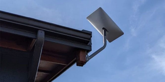 A Starlink dish mounted on a fascia bracket at a roof edge, cabling routed neatly along the trim